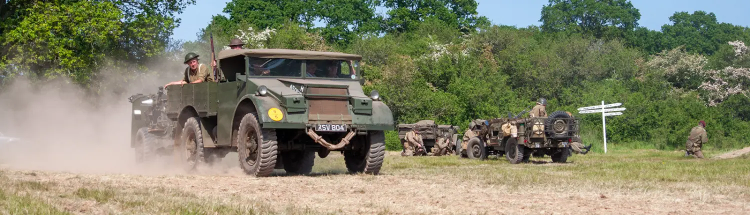 Military vehicle driving through a field, carrying troops and equipment.