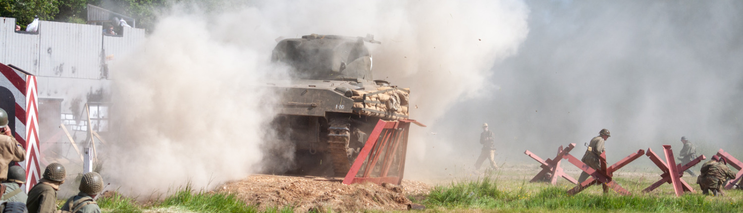 A Sherman tank engulfed in a dense cloud of dust as it succumbs to a powerful explosion while crossing bridge.